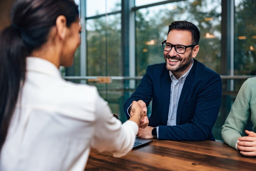 Chefe sorridente apertando a mão de uma cliente feminina, fechando um acordo em uma sala de reunião.