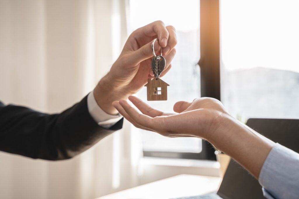 Mão de corretor ou proprietário entregando a chave da casa ao comprador ou inquilino.