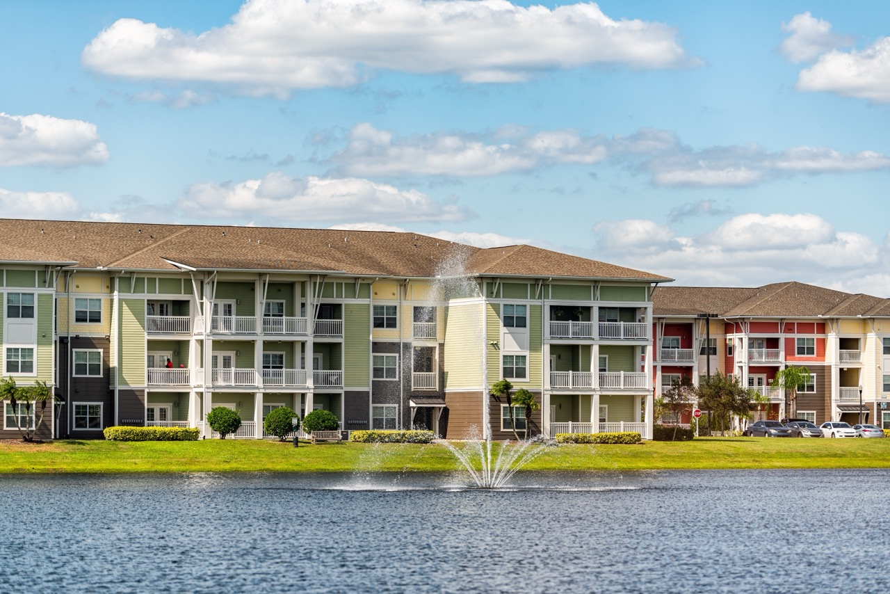 Prédios de apartamentos de luxo de três andares à beira do lago com fonte de água em Orlando, Flórida, com céu azul e nuvens.