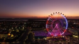 Vista noturna da roda-gigante iluminada do ICON Park em Orlando, com a cidade ao fundo