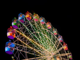 Foto de uma roda-gigante com cabines multicoloridas e luzes brilhantes iluminando a estrutura contra o céu preto da noite.