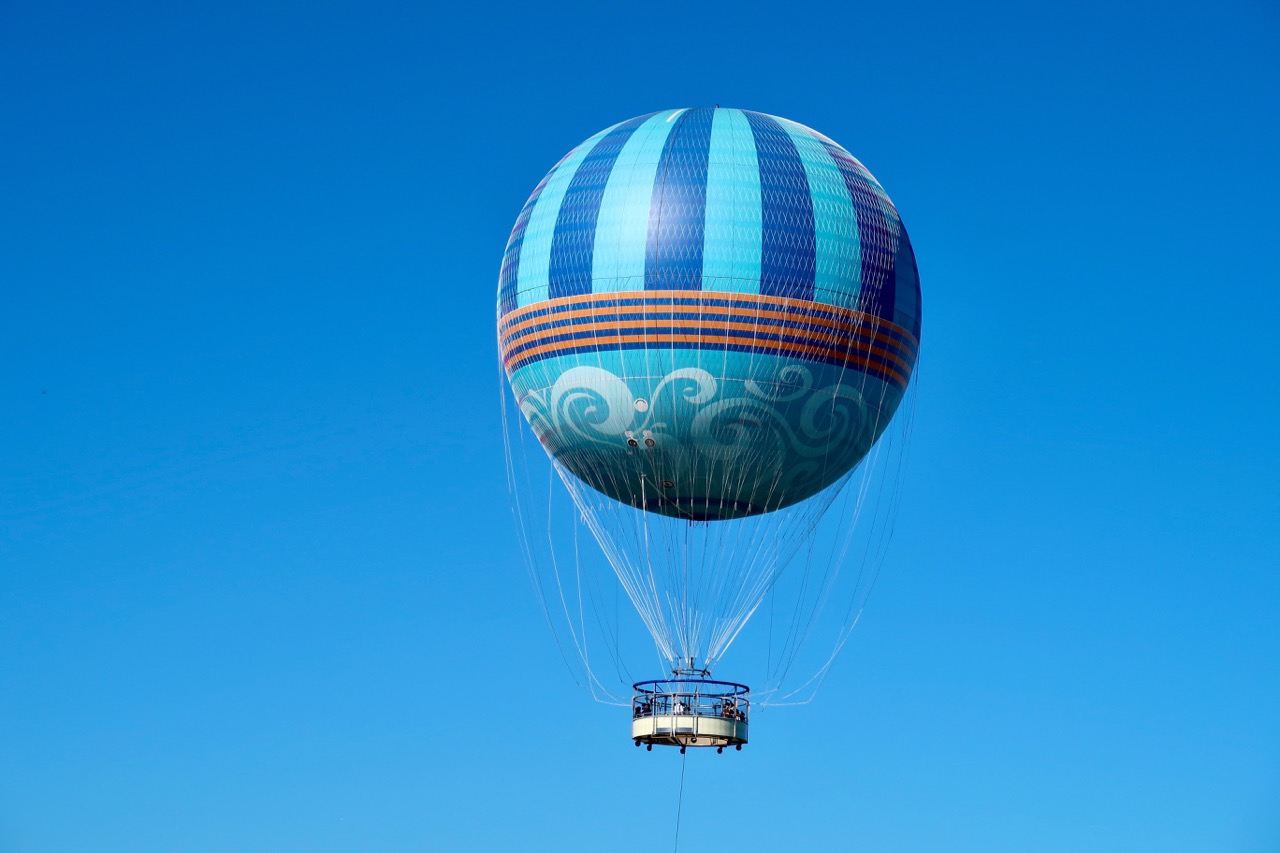 Balão de ar quente azul com detalhes decorativos flutuando no céu claro.