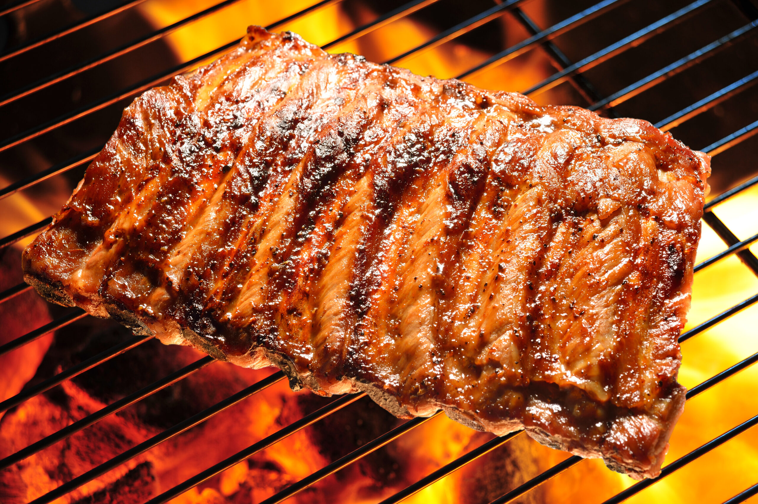 Costela de porco grelhada sobre uma grelha com brasa em chamas ao fundo, com molho caramelizado brilhante.